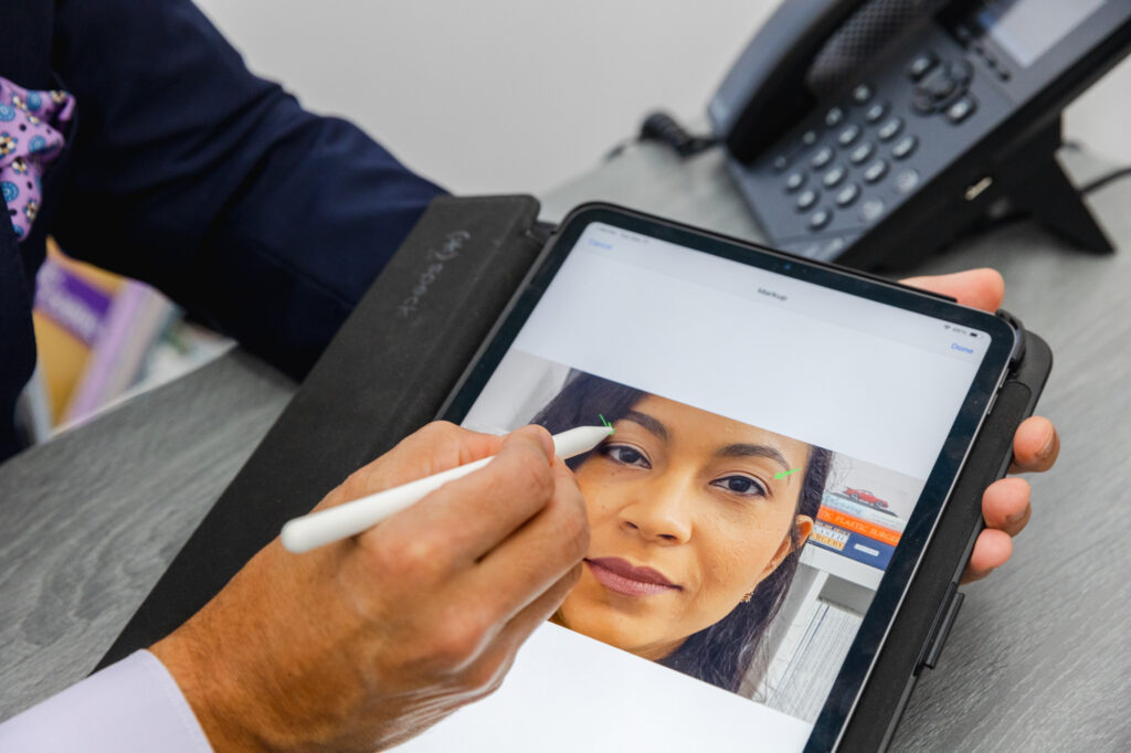Dr. Salas draws on an iPad, which features a close-up image of a female patient's face. He plans out his surgical approach for a brow lift near Miami.