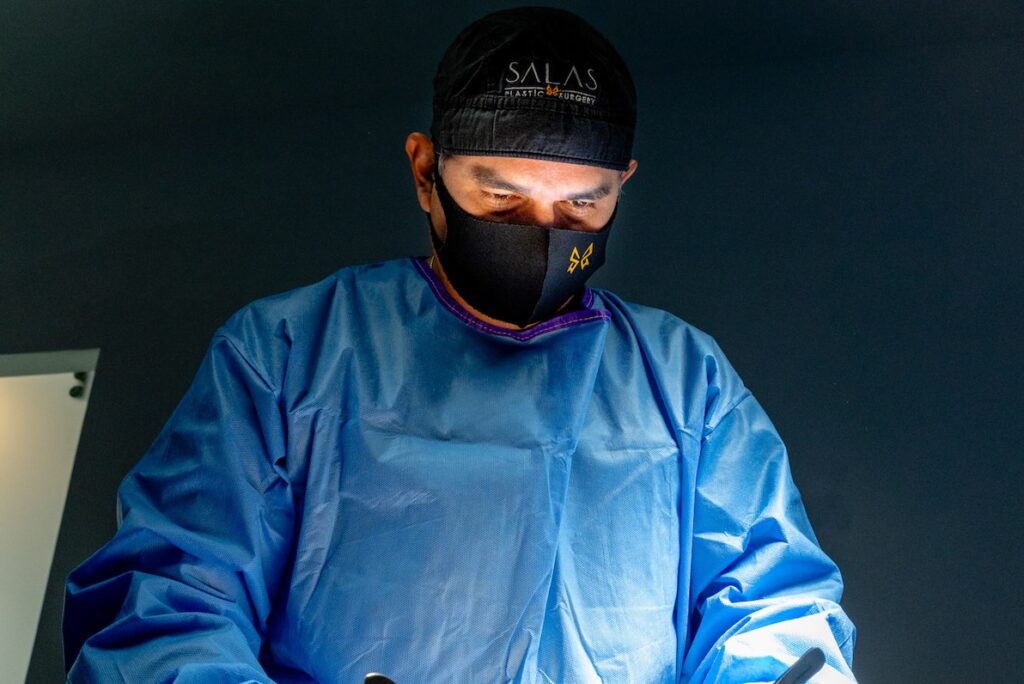 A plastic surgeon in a blue gown and mask performing precise stomach fat removal in Pembroke Pines in a clinical surgical suite.